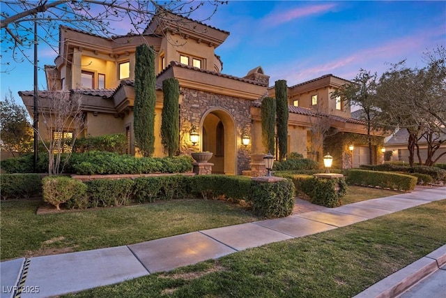 mediterranean / spanish-style home featuring stone siding, a tile roof, a front lawn, and stucco siding