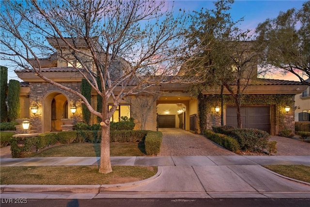 mediterranean / spanish-style house with a garage, stone siding, and decorative driveway