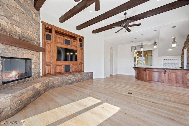 unfurnished living room with light wood finished floors, a fireplace, arched walkways, and beamed ceiling