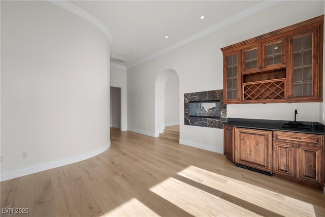 bar with arched walkways, light wood finished floors, ornamental molding, a sink, and baseboards