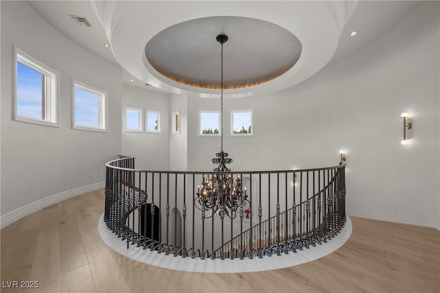 corridor with a raised ceiling, visible vents, an inviting chandelier, an upstairs landing, and hardwood / wood-style floors