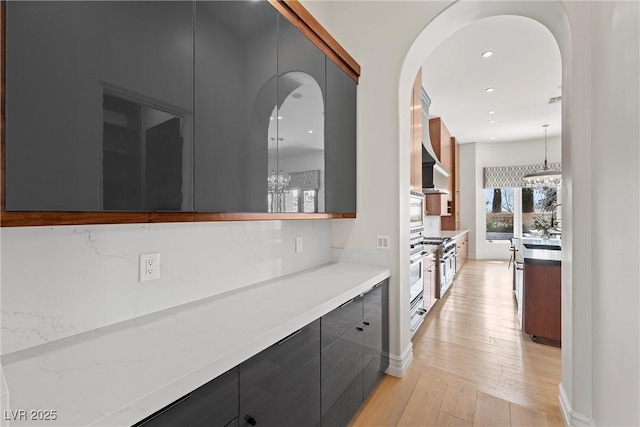 interior space with light wood-style flooring, modern cabinets, white oven, hanging light fixtures, and light countertops