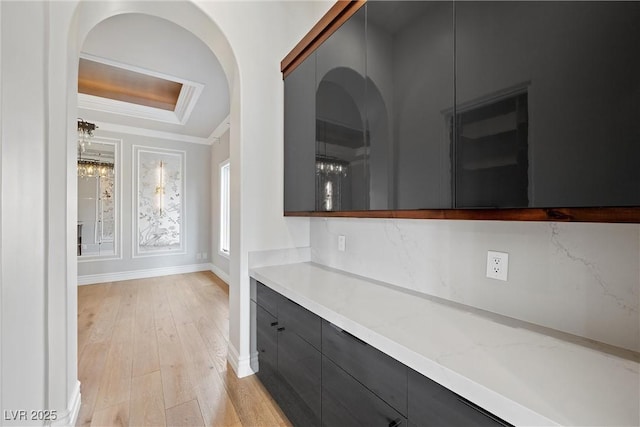 interior space featuring a tray ceiling, crown molding, light wood-style floors, modern cabinets, and baseboards