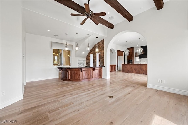 unfurnished living room featuring arched walkways, baseboards, a ceiling fan, light wood-style flooring, and beamed ceiling