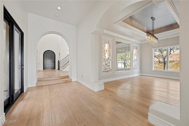 interior space with baseboards, a raised ceiling, stairway, light wood-style floors, and a notable chandelier