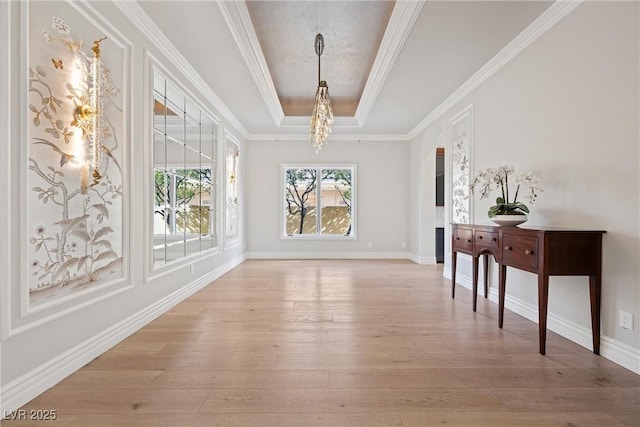 dining space with a notable chandelier, baseboards, light wood-type flooring, a raised ceiling, and crown molding