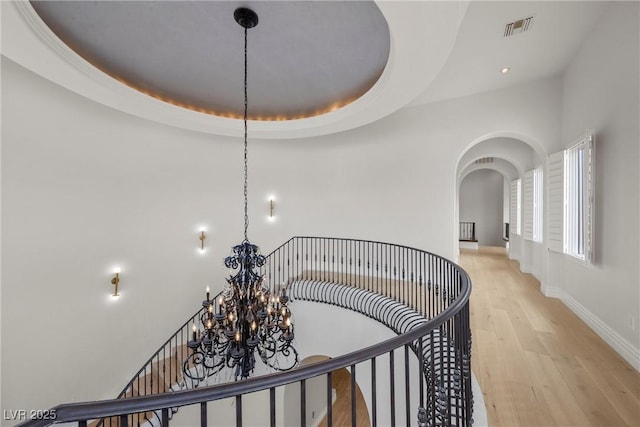 hall with arched walkways, light wood-style flooring, visible vents, baseboards, and a raised ceiling