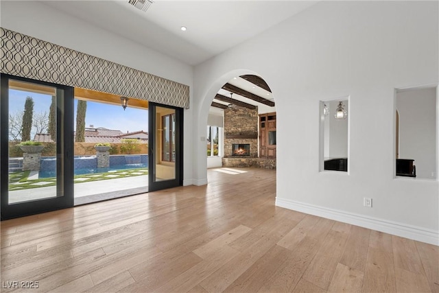 empty room with a stone fireplace, beamed ceiling, wood finished floors, and baseboards