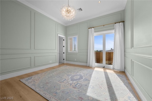 interior space with a chandelier, light wood-style flooring, a decorative wall, visible vents, and ornamental molding