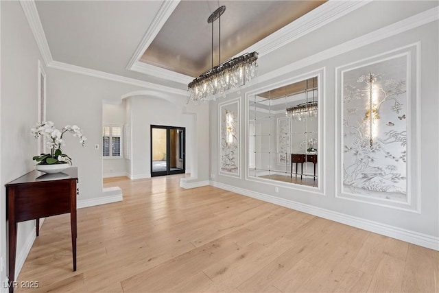 interior space featuring baseboards, ornamental molding, a raised ceiling, and light wood-style floors