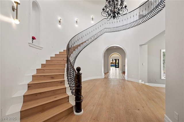 foyer featuring baseboards, arched walkways, a towering ceiling, hardwood / wood-style floors, and a notable chandelier