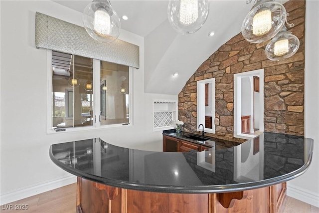 bar featuring light wood-style floors, pendant lighting, a sink, and baseboards