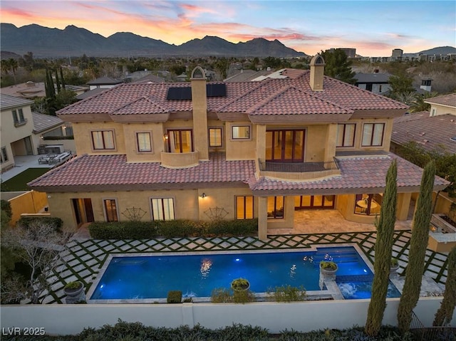 rear view of property with a chimney, solar panels, a mountain view, a balcony, and a tiled roof