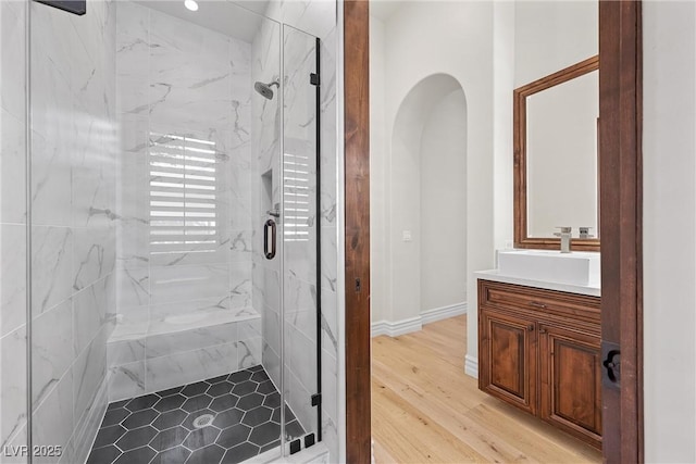 full bathroom featuring a marble finish shower, baseboards, wood finished floors, and vanity