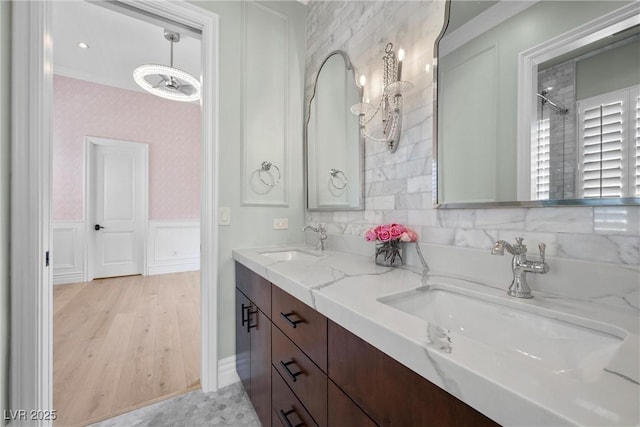 full bath featuring a wainscoted wall, double vanity, a sink, and wallpapered walls