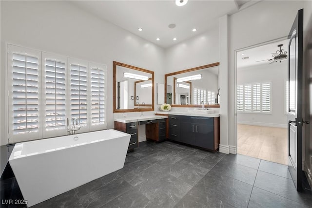 bathroom with baseboards, a high ceiling, a freestanding bath, vanity, and recessed lighting