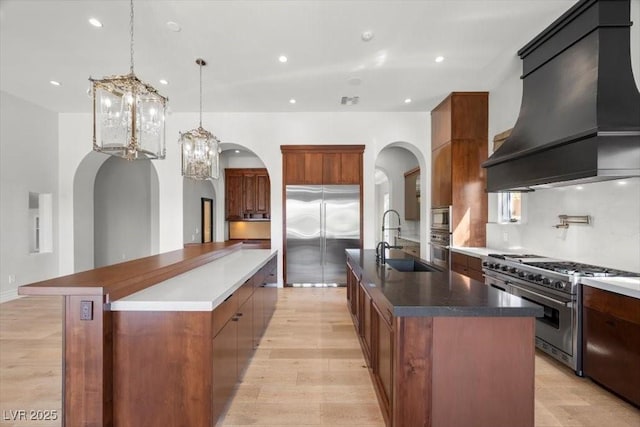 10923 Willow Heights Dr, Las Vegas, NV 89135 - kitchen featuring custom range hood, a large island with sink, built in appliances, arched walkways, and recessed lighting