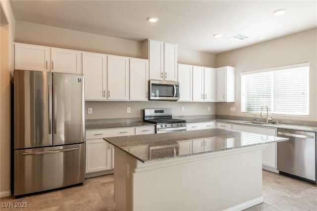 kitchen with appliances with stainless steel finishes, light stone counters, a kitchen island, white cabinets, and sink