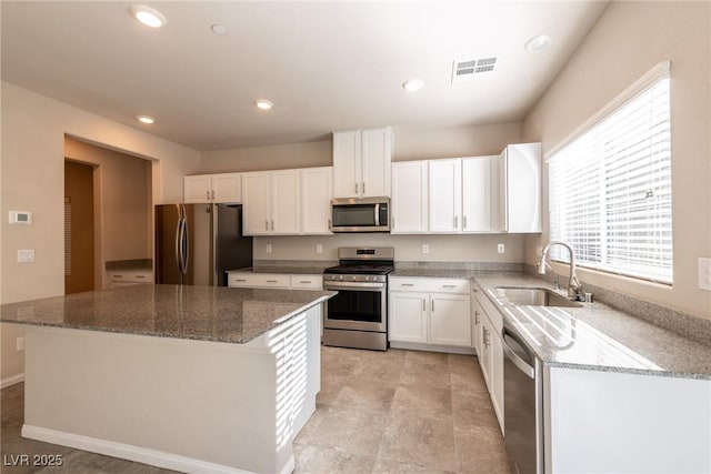 kitchen featuring stainless steel appliances, white cabinets, a center island, and light stone countertops