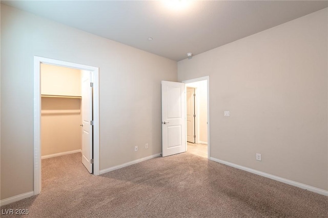 unfurnished bedroom featuring a walk in closet, a closet, and light carpet