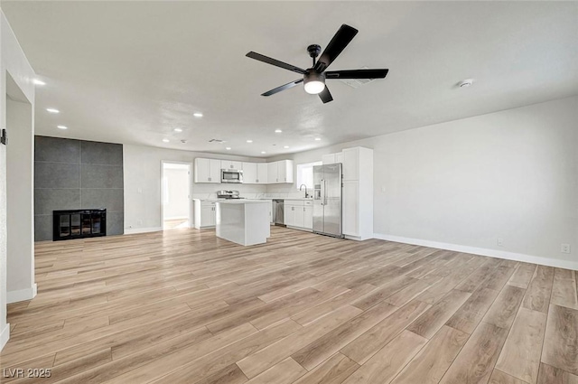 unfurnished living room with ceiling fan, light hardwood / wood-style floors, sink, and a fireplace