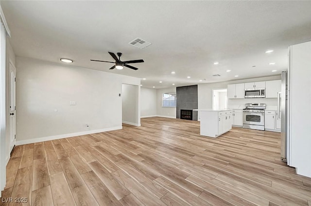 unfurnished living room featuring a tile fireplace, ceiling fan, and light wood-type flooring