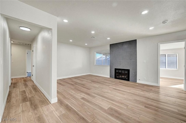 unfurnished living room featuring a tiled fireplace and light hardwood / wood-style flooring