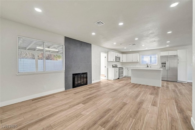 unfurnished living room featuring a tile fireplace, light wood-type flooring, and sink