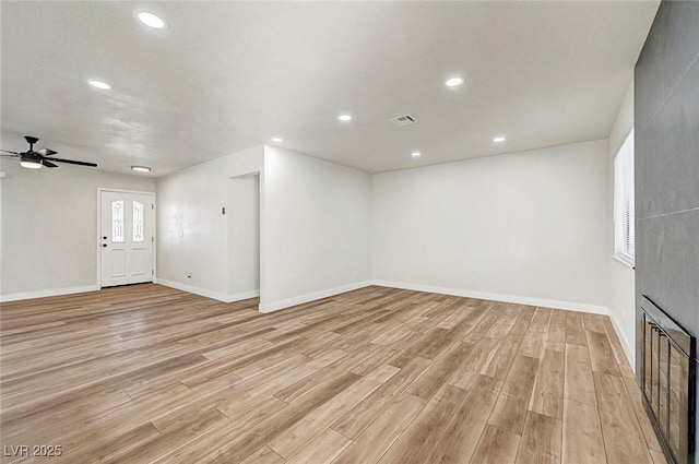 unfurnished living room with a large fireplace, ceiling fan, and light hardwood / wood-style flooring