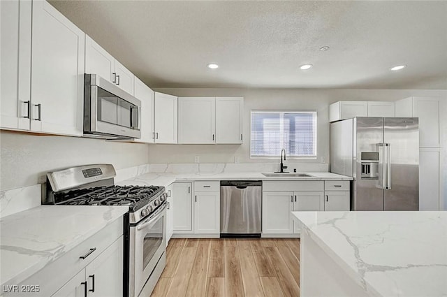 kitchen with appliances with stainless steel finishes, light wood-type flooring, light stone counters, white cabinets, and sink