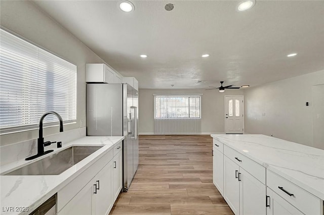 kitchen with light stone counters, stainless steel refrigerator with ice dispenser, white cabinets, ceiling fan, and sink