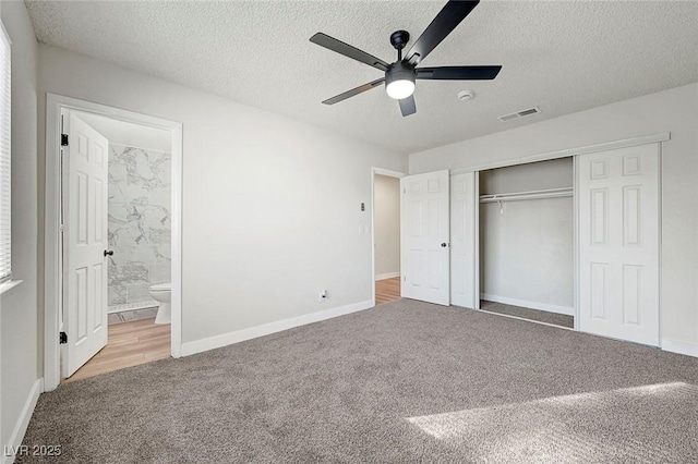 unfurnished bedroom featuring a textured ceiling, ensuite bathroom, a closet, light colored carpet, and ceiling fan