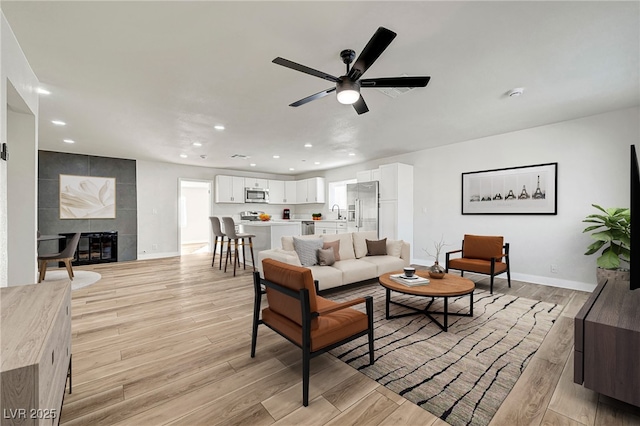 living room with a tiled fireplace, ceiling fan, and sink