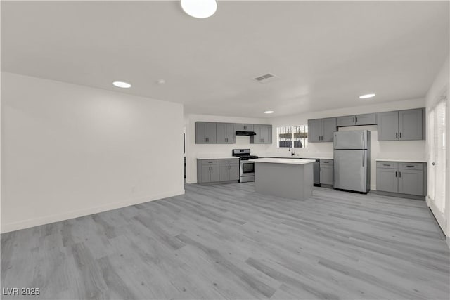 kitchen with appliances with stainless steel finishes, gray cabinetry, light hardwood / wood-style flooring, and a kitchen island