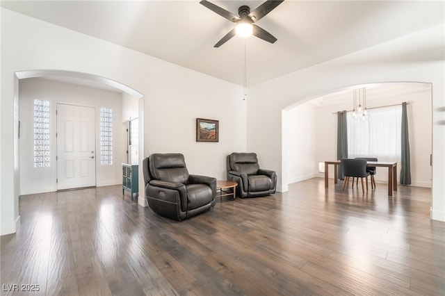 living area featuring ceiling fan with notable chandelier and dark wood-type flooring