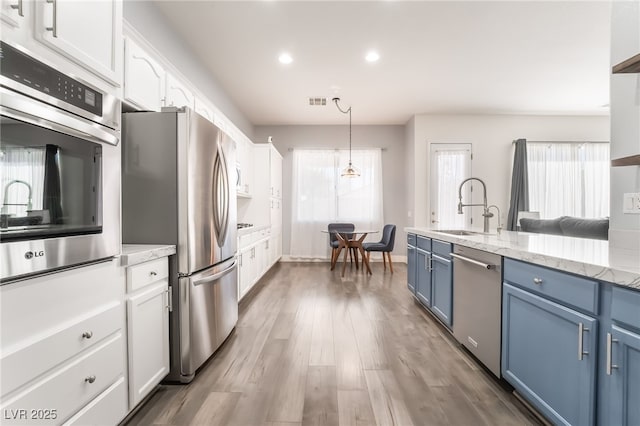 kitchen featuring decorative light fixtures, stainless steel appliances, blue cabinetry, white cabinetry, and sink