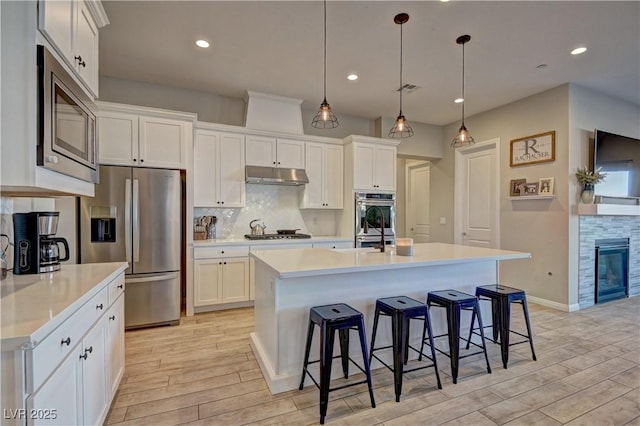 kitchen featuring hanging light fixtures, a center island with sink, backsplash, white cabinetry, and appliances with stainless steel finishes