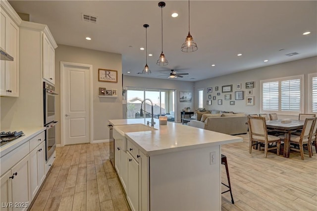 kitchen with ceiling fan, white cabinetry, light wood-type flooring, and a center island with sink