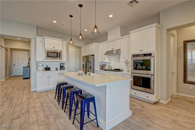 kitchen with stainless steel appliances, a kitchen island with sink, pendant lighting, and white cabinetry