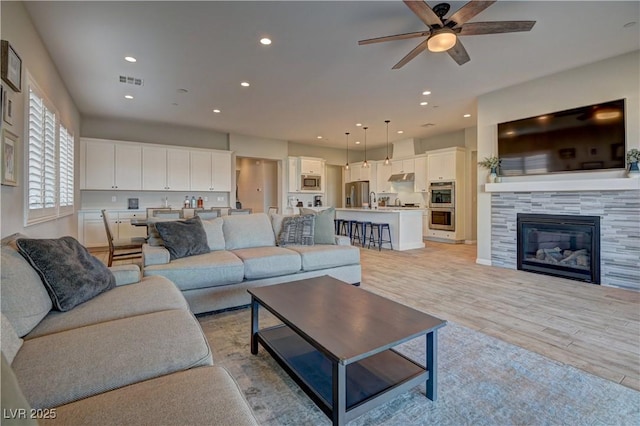 living room featuring ceiling fan, light hardwood / wood-style flooring, sink, and a fireplace