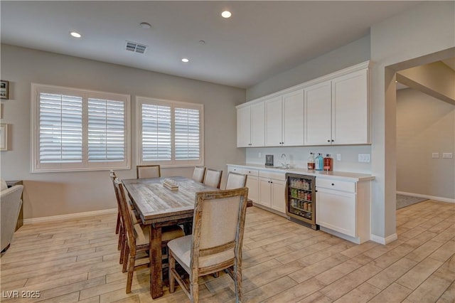 dining area with beverage cooler, indoor wet bar, and light hardwood / wood-style floors