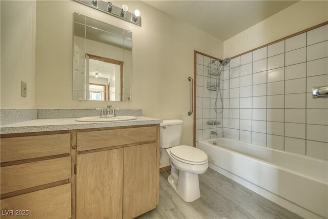 full bathroom with tiled shower / bath, toilet, vanity, and wood-type flooring