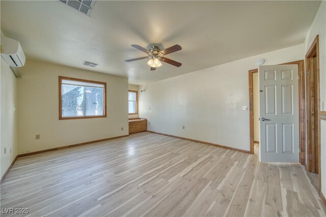 unfurnished bedroom with a wall mounted AC, light wood-type flooring, and ceiling fan