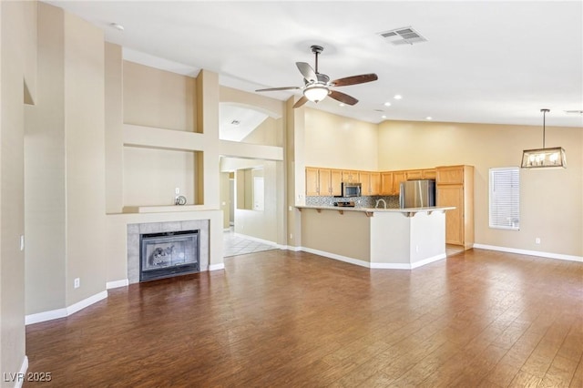 unfurnished living room featuring a tiled fireplace, dark wood-type flooring, lofted ceiling, and ceiling fan with notable chandelier