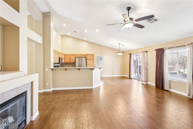 unfurnished living room featuring dark hardwood / wood-style flooring, a tiled fireplace, ceiling fan, and vaulted ceiling