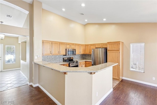 kitchen with kitchen peninsula, stainless steel appliances, backsplash, and light hardwood / wood-style flooring