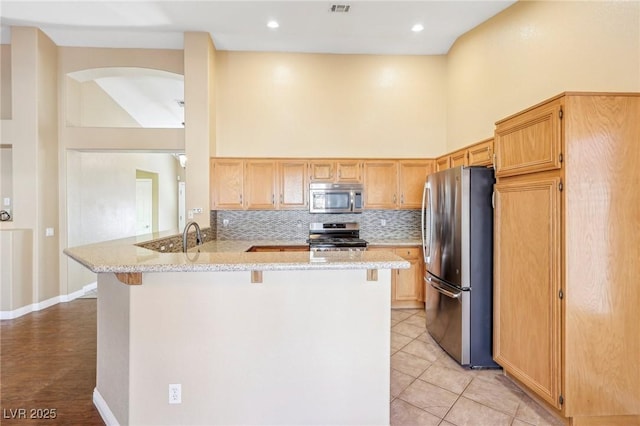 kitchen with stainless steel appliances, tasteful backsplash, kitchen peninsula, light stone countertops, and a high ceiling