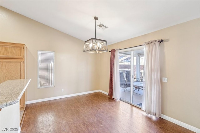 unfurnished dining area with hardwood / wood-style floors, lofted ceiling, and a chandelier