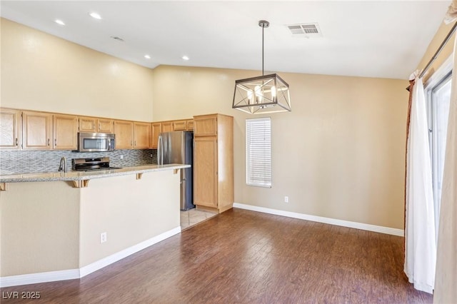 kitchen featuring a kitchen breakfast bar, stainless steel appliances, a notable chandelier, decorative backsplash, and decorative light fixtures