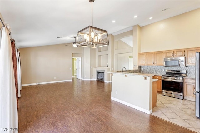 kitchen with appliances with stainless steel finishes, hanging light fixtures, kitchen peninsula, a breakfast bar, and ceiling fan with notable chandelier